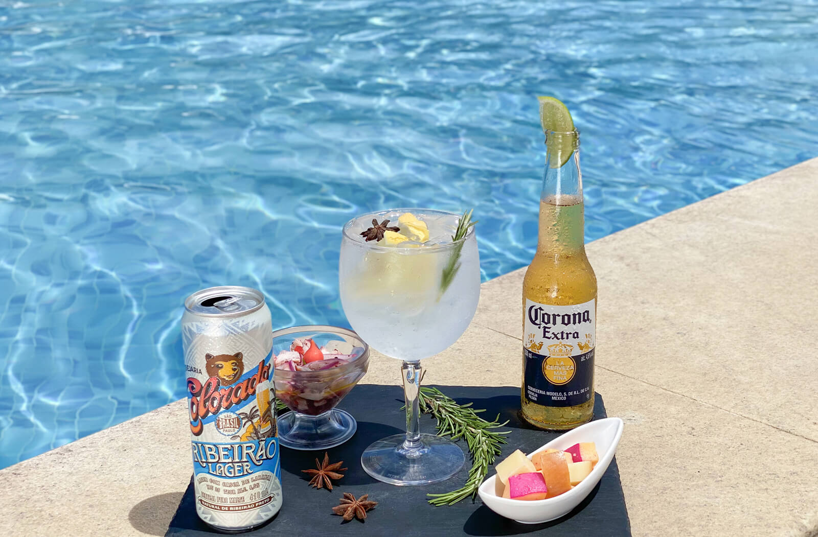foto de uma bandeja servindo duas cervejas, uma corona e outra colorado na borda da piscina, também há um drink feito de vodka e alguns petiscos frios