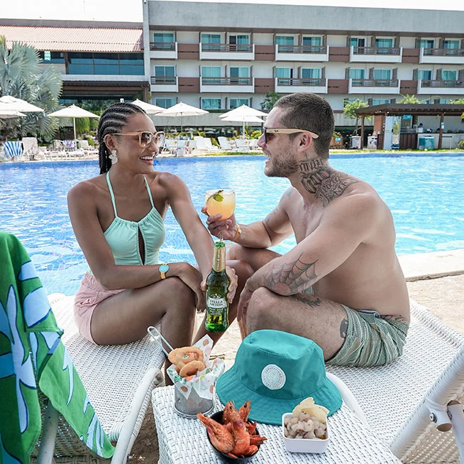 Casal desfrutando de petiscos à beira da piscina no Japaratinga Lounge Resort.