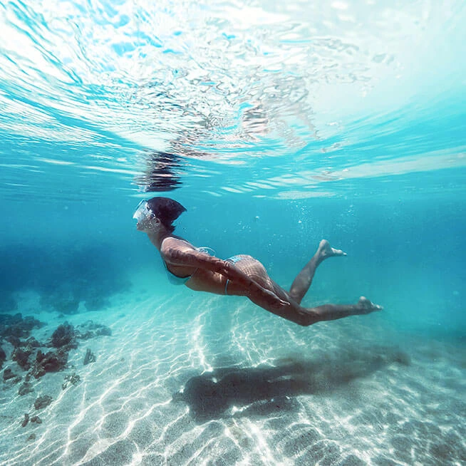 Mulher mergulhando em águas cristalinas das piscinas naturais de Japaratinga com máscara de snorkel, explorando o fundo do mar.