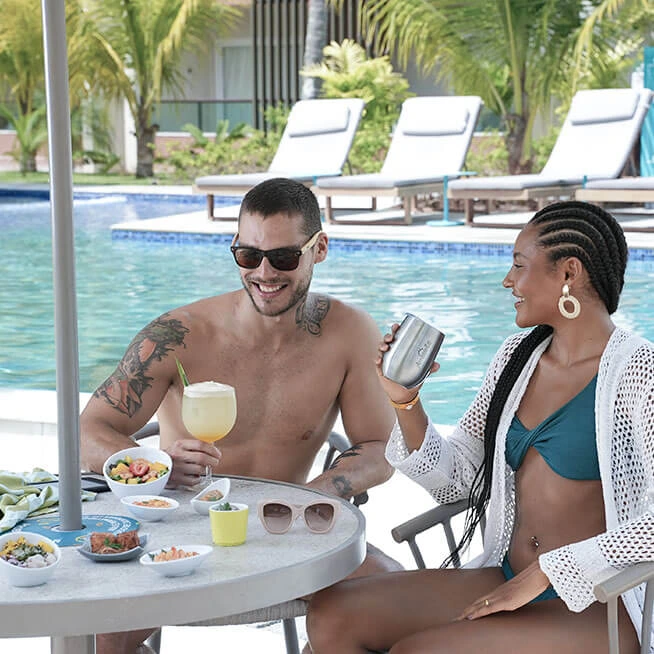 Casal desfrutando de petiscos e bebidas à beira da piscina no Japaratinga Lounge Resort.