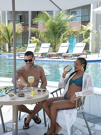 Casal relaxando à beira da piscina do Mângo Bar, próximo aos novos apartamentos da categoria Garden. Desfrutando dos petiscos e drinks exclusivos do resort.