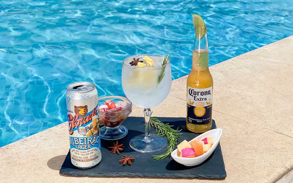 Cerveja long neck Corona Extra ao lado de cerveja lata Colorado, drink exclusivo Japaratinga Lounge Resort e tigelas com queijos e ceviche.