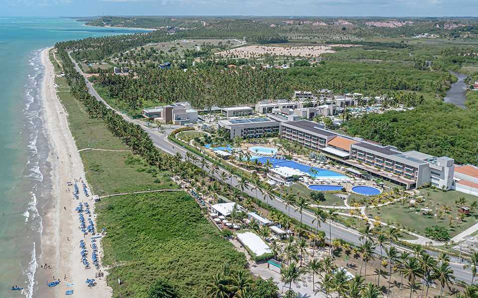 Vista aérea do primeiro All Inclusive Premium do Brasil, o Japaratinga Lounge Resort, com suas acomodações, diversos pontos de consumo e complexo de piscinas, rodeado por uma densa vegetação nativa e à beira mar.