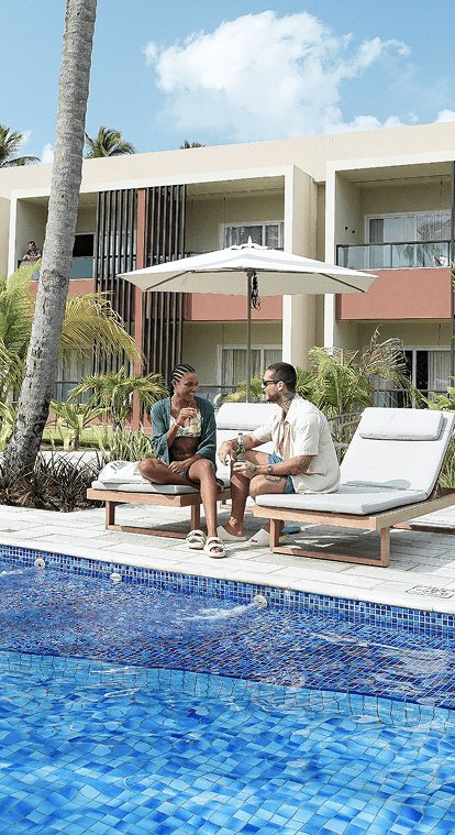 Casal desfrutando de bebidas e petiscos em espreguiçadeira ao lado da piscina do Mangô Bar, próximo às novas categorias de apartamentos Garden, do Japaratinga Lounge Resort