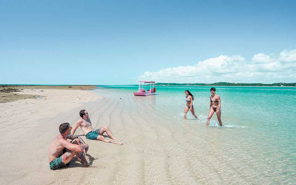 Quatro amigos descansam ao lado de jangada na prainha da Croa de São Bento.